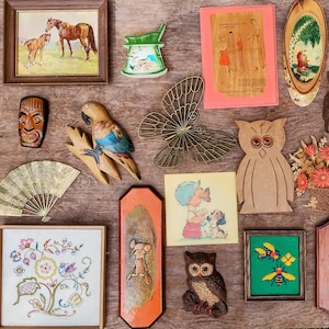May include: A collection of vintage decorative items, including framed artwork of horses, a carved wooden parrot, a metal butterfly, a wooden owl, and a framed embroidery piece. The items are arranged on a wooden surface.