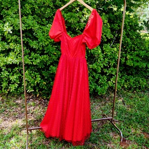 May include: A red vintage dress with a sweetheart neckline and puff sleeves. The dress is made of a sheer fabric with a polka dot pattern and has a lace trim at the hem.