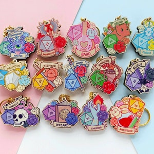 Peut inclure: Un ensemble de 12 porte-clés en bois représentant différentes classes de personnages de Donjons et Dragons. Chaque porte-clés comporte un dé à 20 faces, une icône de personnage et des accents floraux. Les classes incluent Barbare, Barde, Clerc, Druide, Guerrier, Moine, Paladin, Ranger, Voleur, Sorcier, Sorcier et Magicien.