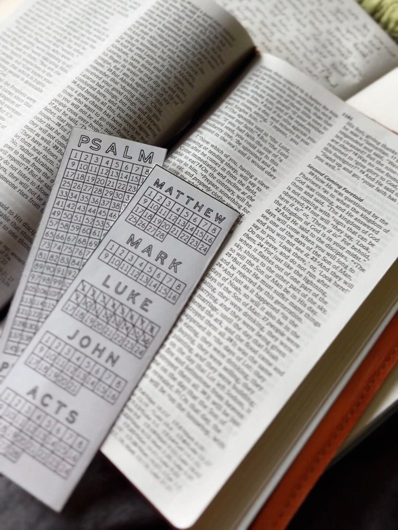 K&ouml;nnte beinhalten: Nahaufnahme einer Bibel, die auf das Neue Testament ge&ouml;ffnet ist. Die Seiten sind abgenutzt und haben eine gelbliche T&ouml;nung. Es befinden sich mehrere Lesezeichen in der Bibel, jedes mit einem anderen Buch der Bibel bedruckt: Psalmen, Matth&auml;us, Markus, Lukas, Johannes und Apostelgeschichte.