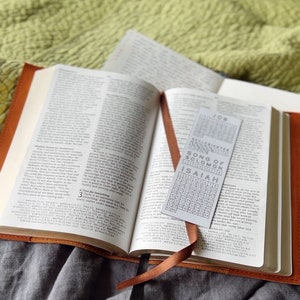 K&ouml;nnte beinhalten: Eine braune, ledergebundene Bibel mit einem Lesezeichen. Das Lesezeichen ist eine wei&szlig;e Karte mit einem Zahlenraster und den Namen der B&uuml;cher der Bibel: Hiob, Prediger Salomo, Hohelied Salomos und Jesaja.