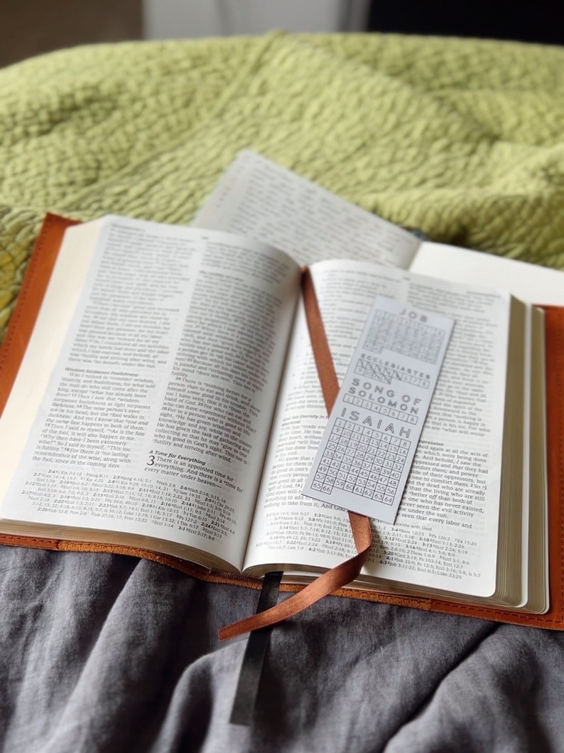 K&ouml;nnte beinhalten: Eine braune, ledergebundene Bibel mit einem Lesezeichen. Das Lesezeichen ist eine wei&szlig;e Karte mit einem Zahlenraster und den Namen der B&uuml;cher der Bibel: Hiob, Prediger Salomo, Hohelied Salomos und Jesaja.