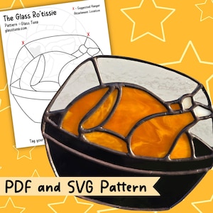 Könnte beinhalten: Ein Buntglas-Suncatcher, der ein gebratenes Hähnchen in einer Schüssel darstellt, mit bernsteinfarbenen, weißen und klaren Glasteilen und dunklen Lötlinien. Daneben liegt ein Papiermuster mit dem Titel The Glass Ro'tissie und SVG- sowie PDF-Beschriftungen.
