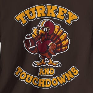 May include: A brown t-shirt featuring a cartoon turkey wearing a football helmet and holding a football. The text "TURKEY and TOUCHDOWNS" is arched above and below the turkey illustration in yellow and orange.