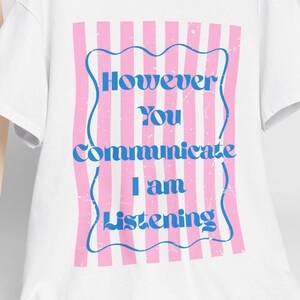 Può includere: Una t-shirt bianca a maniche corte con una grafica rettangolare a righe verticali rosa e bianche con un bordo blu ondulato. Il testo "However You Communicate I am Listening" è stampato in blu. È incluso un cappellino da baseball bianco.