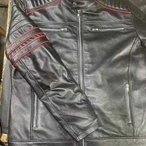 May include: Black leather jacket with red accent stripes on the shoulders and sleeves. The jacket has a zippered front, multiple zippered pockets, and a stand-up collar. The jacket is a classic motorcycle style.