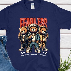 May include: Navy blue t-shirt with a graphic of three cartoon bears in hoodies and jeans, with the word "FEARLESS" in red. The shirt also has the text "SPREAD LOVE - DROP BEATS - PEACE OUT". A pair of blue jeans is next to the shirt.