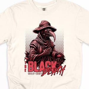 May include: Cream-colored t-shirt featuring a red graphic of a plague doctor with a long beak and hat. The text "BLACK DEATH" and the years "1347-1351" are printed in red below the illustration.