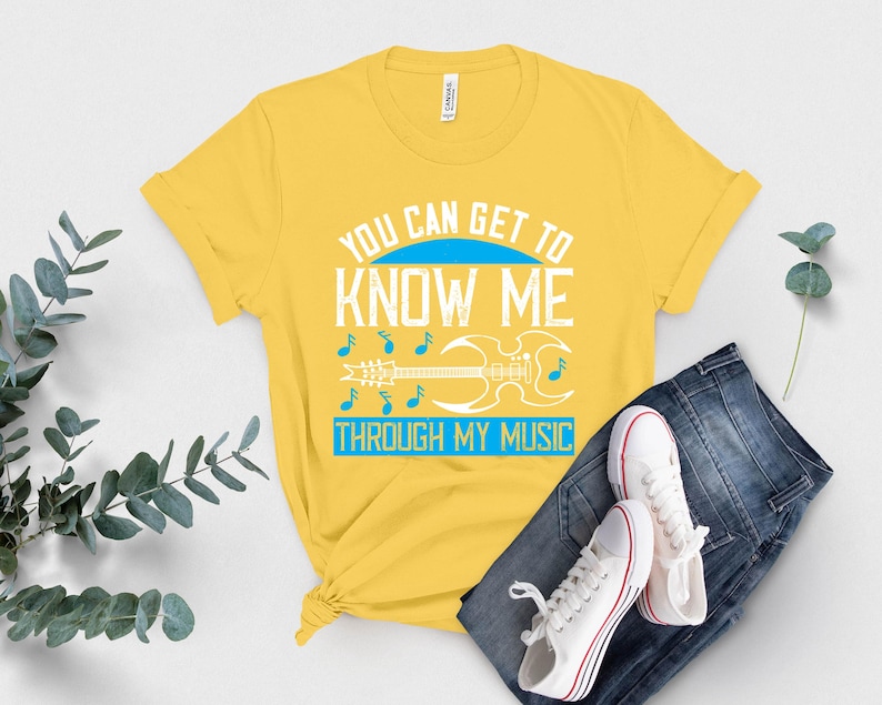 K&ouml;nnte beinhalten: Gelbes T-Shirt mit dem Text "YOU CAN GET TO KNOW ME THROUGH MY MUSIC" in Wei&szlig; und Blau. Das Design umfasst Noten und eine Gitarre. Das Shirt wird mit einer blauen Jeans und wei&szlig;en Turnschuhen kombiniert.