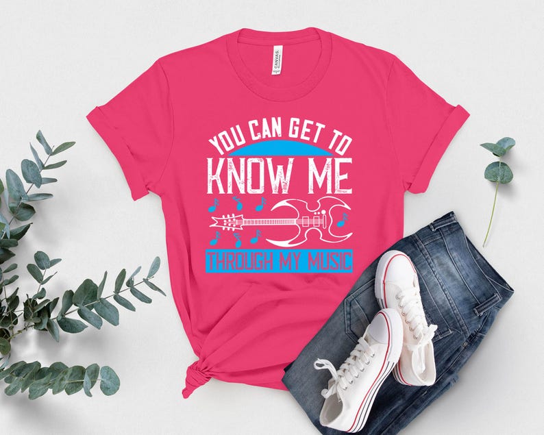 K&ouml;nnte beinhalten: Ein leuchtend pinkfarbenes T-Shirt mit dem Text "YOU CAN GET TO KNOW ME THROUGH MY MUSIC" in Wei&szlig; und Blau. Eine wei&szlig;e Gitarrengrafik ist darunter zentriert. Das Shirt wird mit blauen Jeans und wei&szlig;en Turnschuhen kombiniert.