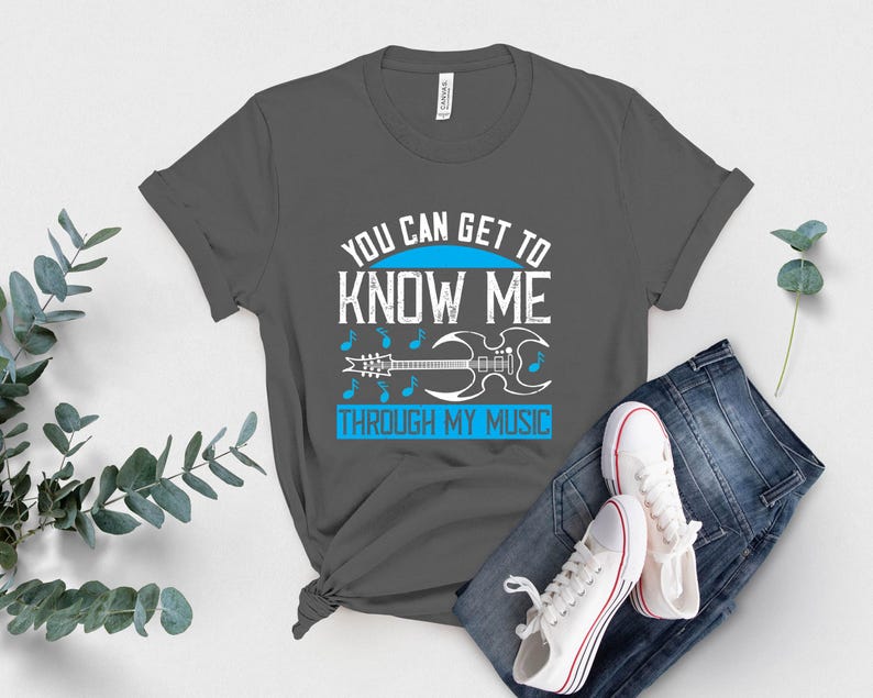 K&ouml;nnte beinhalten: Ein graues T-Shirt mit dem Text "YOU CAN GET TO KNOW ME THROUGH MY MUSIC" in Wei&szlig; und Blau. Das Design umfasst Noten und eine Gitarren-Grafik. Das Shirt wird mit blauen Jeans und wei&szlig;en Turnschuhen kombiniert.