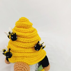 May include: A handmade crochet gnome with a yellow beehive-shaped hat and three attached bees. The gnome has a white beard, a tan nose, and black and yellow striped bee accents. The gnome is a whimsical decorative item.