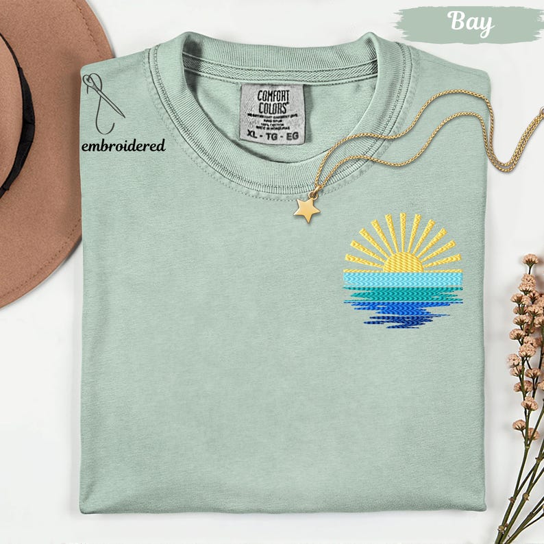 a light green t-shirt with a sun embroidered design on the front, along with a gold star pendant and a brown hat.