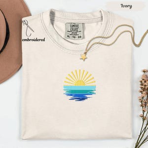 a white t-shirt with a sun embroidered design on it, along with a gold star pendant and a brown hat.