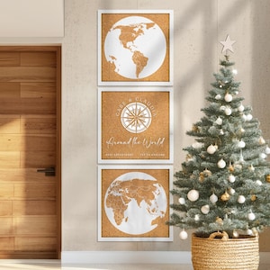 May include: Three framed corkboard prints with white borders. Two prints feature a white world map, and the center print has a compass design with the text "Gabe & Claudia Around the World". A decorated Christmas tree is in the background.
