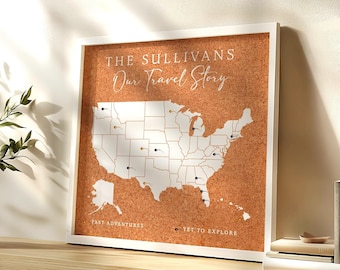 May include: A square cork board map of the United States in a white frame. The text reads THE SULLIVANS Our Travel Story, PAST ADVENTURES, and YET TO EXPLORE. The map features white state outlines on a brown cork background with various colored push pins.