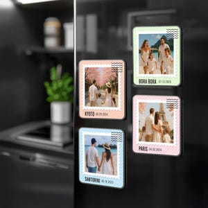 以下が含まれることがあります： 家族写真と旅行先が写った長方形のマグネット4つ。各マグネットは異なる色の縁取りがあり、場所と日付が記載されています。行き先はボラボラ、京都、サントリーニ、パリです。