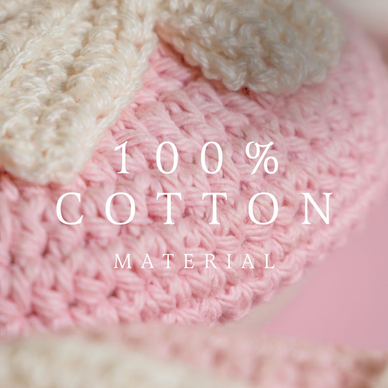 May include: Close-up of a handmade crochet item in soft pink and cream colors. The text "100% COTTON MATERIAL" is displayed in white. The item appears to be a hat or a similar accessory, showcasing a textured stitch.