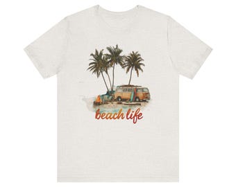 May include: A light gray t-shirt featuring a watercolor illustration of a beach scene. The design includes palm trees, a vintage van with surfboards, and a campfire. The words "beach life" are written in a cursive font.