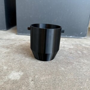 May include: A black plastic cup with a rounded bottom and two small handles on the sides.