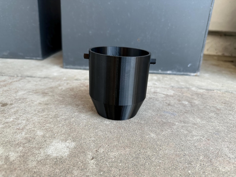 May include: A black plastic cup with a rounded bottom and two small handles on the sides.