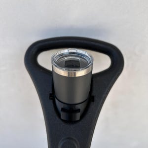 May include: A black travel mug with a stainless steel lid and a black plastic holder. The holder is attached to a black handle.