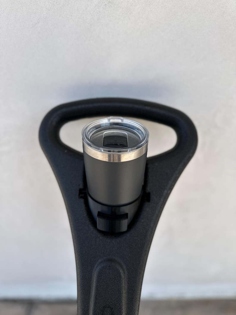 May include: A black travel mug with a stainless steel lid and a black plastic holder. The holder is attached to a black handle.