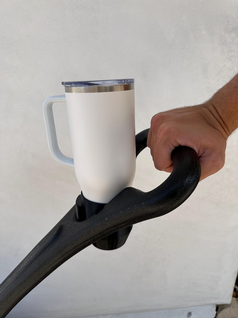 May include: White travel mug with a black handle, attached to a black stroller handle.