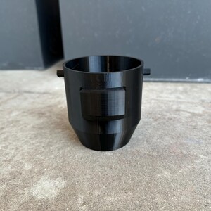 May include: A black plastic 3D printed funnel with a rectangular opening on the side.