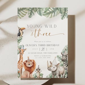 以下が含まれることがあります： サファリをテーマにした誕生日招待状。オオハシ、キリン、ライオン、ミーアキャット、サイ、シマウマの水彩イラストが特徴です。「Young Wild & Three」の文字とパーティーの詳細が含まれています。