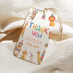 Könnte beinhalten: Ein rechteckiges Geschenk-Etikett mit einer Aquarell-Illustration verschiedener Tiere, darunter ein Affe, eine Giraffe, ein Löwe und ein Tiger. Das Etikett trägt die Aufschrift "THANK YOU" in bunten Buchstaben, mit zusätzlichem Text darunter. Eine natürliche Schnur ist befestigt.