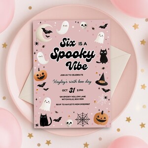 Peut inclure: Une invitation rose pour une f&ecirc;te d'Halloween avec le texte "Six is a Spooky Vibe". L'invitation comprend des illustrations de fant&ocirc;mes, de chauves-souris, de citrouilles et d'un chat noir. L'invitation est pour le sixi&egrave;me anniversaire d'Hayley, le 31 octobre.