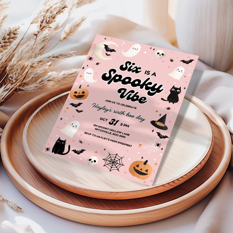 Peut inclure: Une invitation rose sur le th&egrave;me d'Halloween avec le texte "Six is a Spooky Vibe". L'invitation comprend des illustrations de fant&ocirc;mes, de chauves-souris, de citrouilles et un chapeau de sorci&egrave;re. L'invitation est sur un plateau en bois.