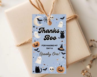 May include: A light blue Halloween gift tag with the words "Thanks Boo" and "For making my day a Spooky One!" surrounded by illustrations of ghosts, bats, pumpkins, and a black cat. The tag is tied to a wrapped gift with twine.