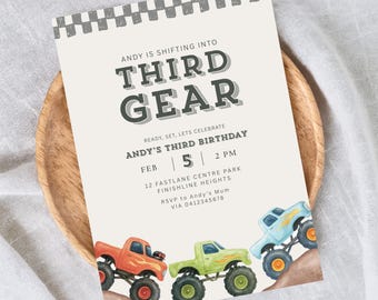 May include: A birthday invitation with the text "ANDY IS SHIFTING INTO THIRD GEAR" and "ANDY'S THIRD BIRTHDAY". The invitation features illustrations of three monster trucks in orange, green, and blue, climbing a dirt hill.