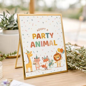 May include: A framed sign with the text "ADOPT A PARTY ANIMAL" in colorful letters. The sign features cartoon animals: a giraffe, cat, fox, and lion, all wearing party hats and holding balloons and a cake. The frame is gold.