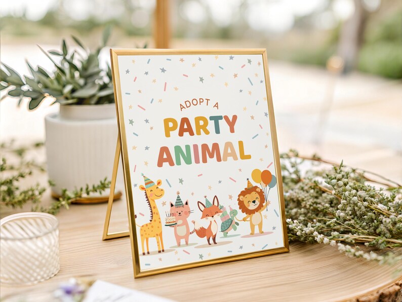 May include: A framed sign with the text "ADOPT A PARTY ANIMAL" in colorful letters. The sign features cartoon animals: a giraffe, cat, fox, and lion, all wearing party hats and holding balloons and a cake. The frame is gold.