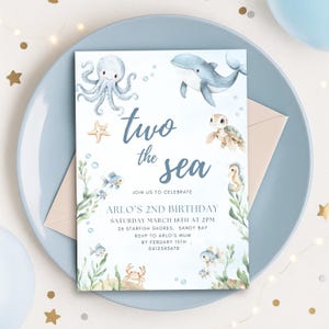 Puede incluir: Una tarjeta de invitación azul claro con ilustraciones de acuarela de criaturas marinas, incluyendo un pulpo, una ballena y una tortuga. El texto dice "two the sea" y anuncia el segundo cumpleaños de Arlo, con fecha, hora y lugar.