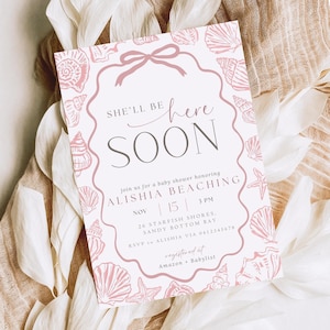 Op de afbeelding: Een uitnodiging voor een babyshower met een roze schelpenrand en strik. De tekst luidt "She'll be here soon" en nodigt gasten uit om Alishia Beaching op 15 november om 15.00 uur te vieren. RSVP-details zijn inbegrepen.