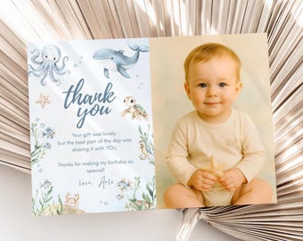 May include: A baby's birthday thank you card with a watercolor illustration of sea creatures and the words "thank you." The card features a photo of a baby holding a starfish. The text reads, "Your gift was lovely, but the best part of the day was sharing it with YOU."