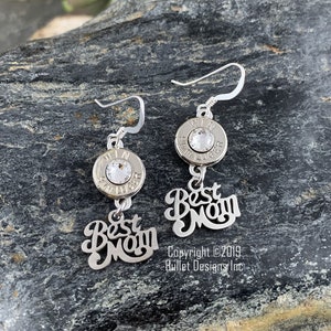 May include: Silver earrings with a bullet casing and a crystal charm. The earrings are adorned with the words "Best Mom" in a cursive font.