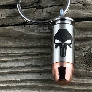 May include: A silver-colored bullet-shaped keychain with a copper base and a black skull design. The keychain has a silver ring for attaching keys. The text "Copyright © 2019 Bullet Designs Inc" is visible.