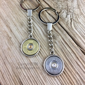 May include: Two keychains with a bullet casing design. One is gold with a 20 GA inscription and the other is silver with a Winchester 20 GA inscription and a rhinestone.