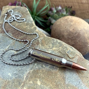 May include: A silver bullet necklace with a silver chain. The bullet is engraved with the words "Customize Me".