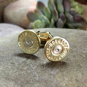 May include: A pair of gold cufflinks made from repurposed .338 Lapua Magnum Hornady rifle casings. The casings are polished and have the brand name and caliber printed on them.