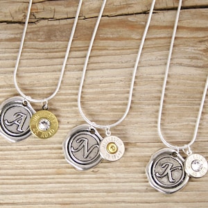 May include: Three silver necklaces with a silver charm featuring a letter and a gold bullet charm. The letters are A, N, and K.
