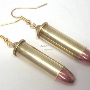 May include: A pair of gold bullet earrings with copper tips. The earrings are made from real bullet casings and have a gold hook.