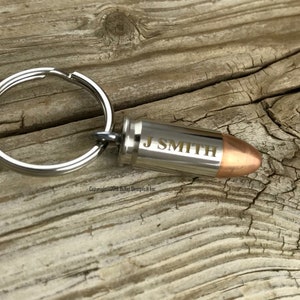 May include: A silver bullet keychain with a copper tip. The bullet is engraved with the name "J Smith".