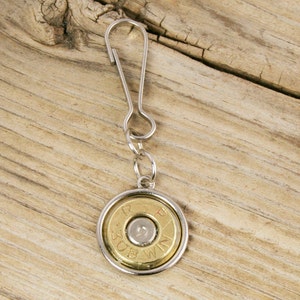 May include: A silver key chain with a round, gold-colored charm featuring a spent .308 Winchester bullet casing. The charm has a silver rim and the bullet casing has the text "308 WIN" printed on it.