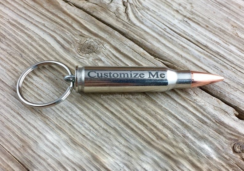 May include: A silver bullet keychain with a key ring and a copper tip. The bullet is engraved with the text "Customize Me".